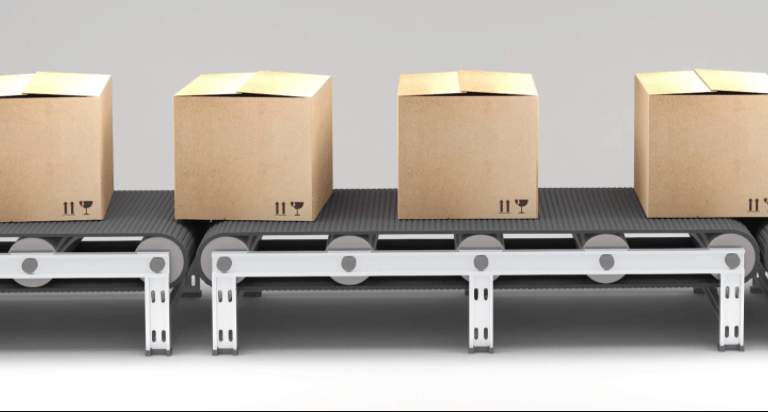 Four closed cardboard boxes are lined up on a conveyor belt, ready for shipping or processing. The background is plain and neutral.