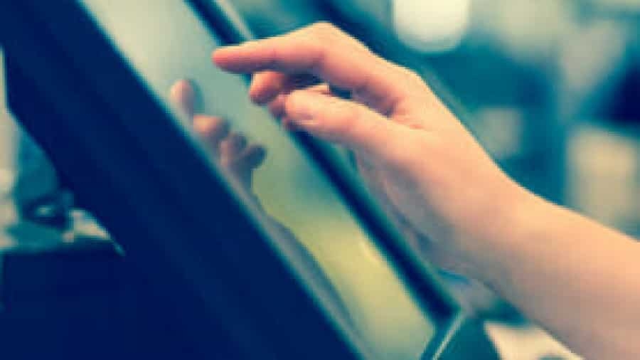 A close-up of a persons hand using a touchscreen device, with a finger touching the screen. The background is blurred.