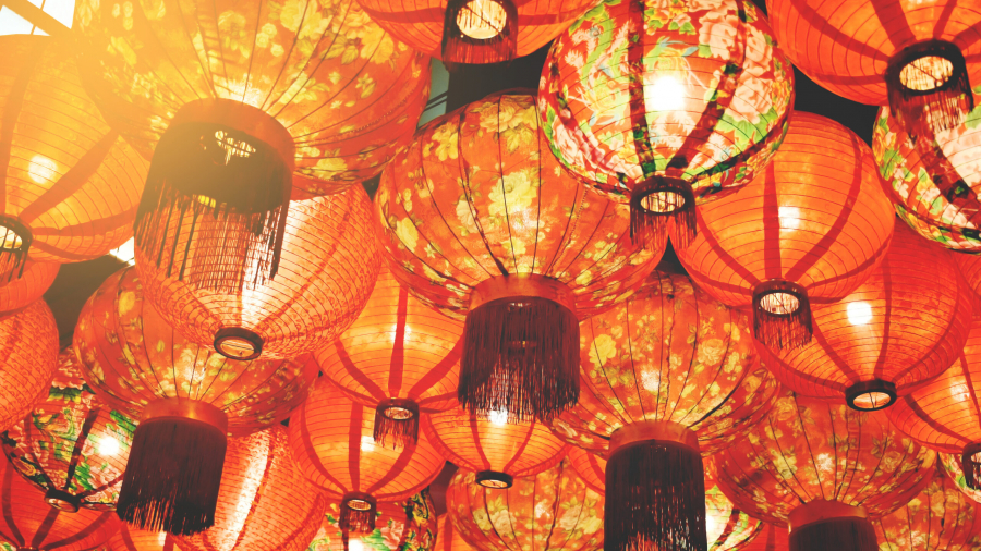 A cluster of traditional red paper lanterns with floral patterns and tassels, hanging closely together and glowing warmly, creating a festive and vibrant atmosphere.