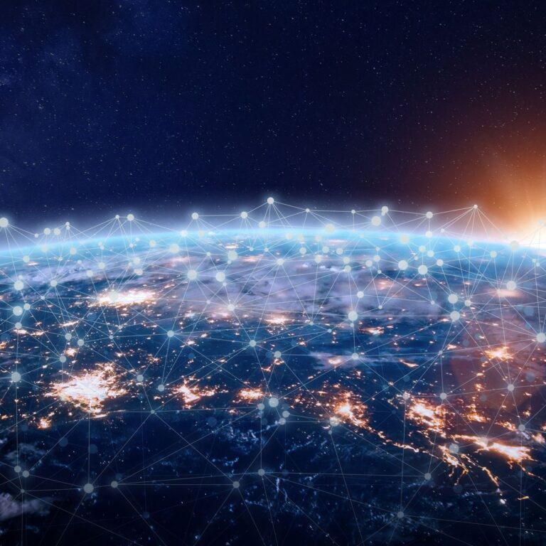 View of Earth from space at sunrise, showing bright city lights and a network of connected points and lines across the surface, symbolizing global communication and connectivity.