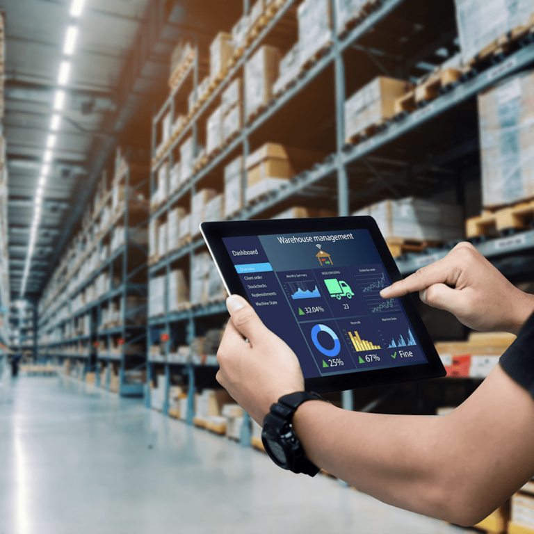 Person using a tablet displaying warehouse automation technologies while standing in a large warehouse with tall shelves filled with boxes and packages.