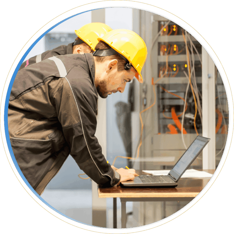 Two workers wearing yellow hard hats and dark jackets use a laptop in front of an open server rack, managing visible cables in a technical setting—demonstrating the power of Dynamics 365 Field Service for efficient operations.