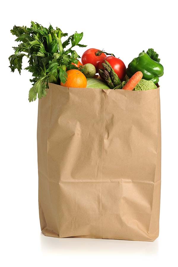 A brown paper grocery bag filled with fresh produce—celery, tomatoes, an orange, lettuce, asparagus, green bell pepper, carrot, and cabbage—sits against a white background, symbolizing the efficiency of transportation network optimization in delivery.
