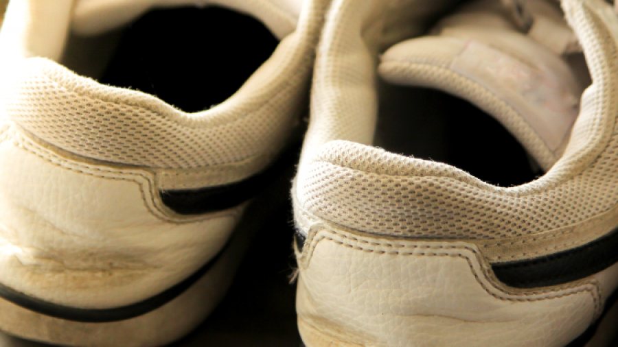 A close-up of the back of a pair of white sneakers with black accents, showing signs of wear and light dirt marks, placed side by side on a surface.
