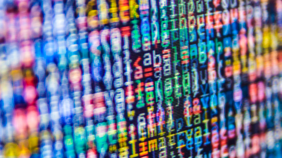 A close-up of a computer screen displaying colorful, blurred lines of code in various programming languages, with characters and symbols in shades of blue, red, green, and yellow.