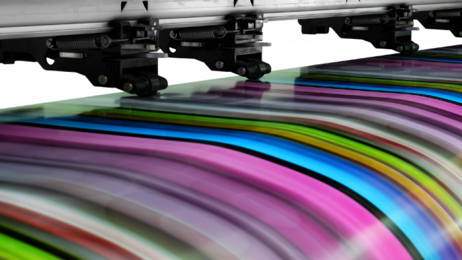 A large industrial printer prints a vibrant, multicolored pattern with stripes of pink, green, blue, yellow, and black on glossy material.