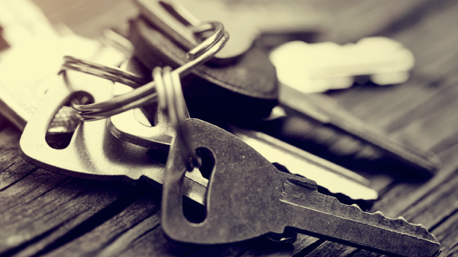 A close-up image of a set of metal keys on a keyring resting on a wooden surface, with a soft, warm light shining from the left side.