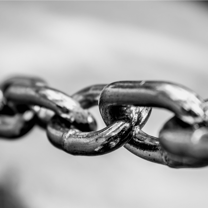 Close-up, black and white photo of metal chain links, with one link in sharp focus and the others fading into a blurred background.