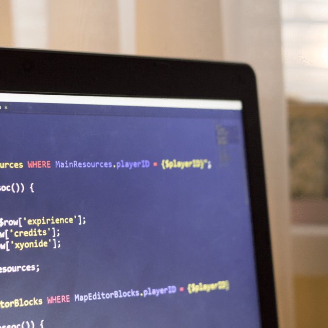 A close-up of a laptop screen displaying code with syntax highlighting in a text editor, set against a softly lit background with curtains and sunlight.