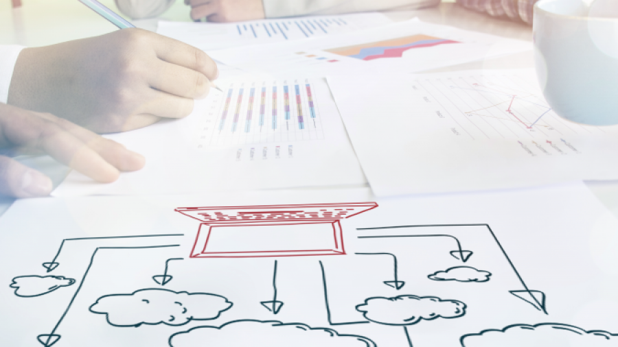 Three people sit at a table with documents, charts, and a coffee cup, discussing a mind map diagram featuring a central box connected to several clouds by arrows.