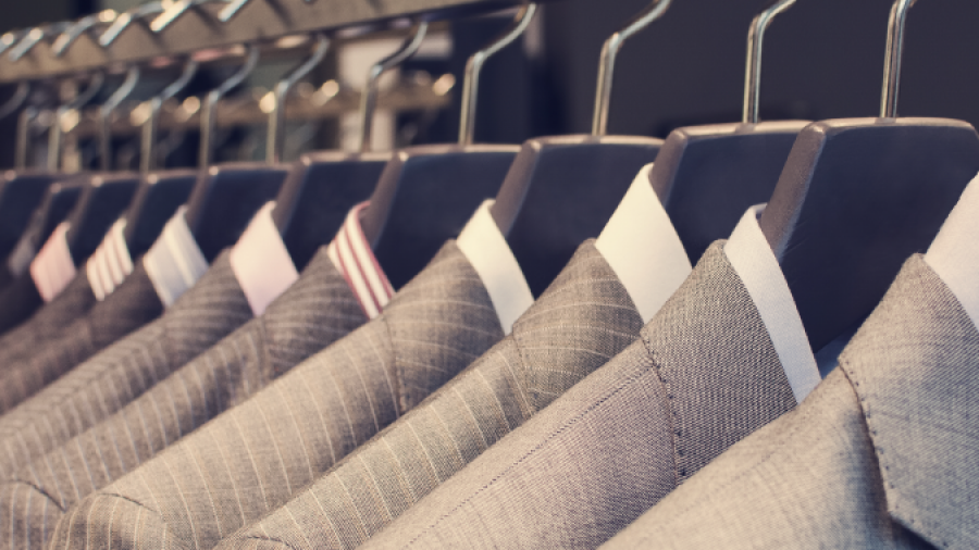 A row of neatly hung mens suit jackets in various shades of grey and patterns on metal hangers, displayed on a rack in a clothing store.