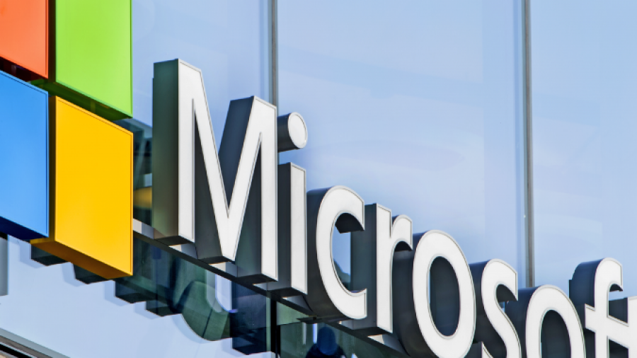 The Microsoft logo featuring a colorful window symbol and the word Microsoft in large letters is displayed on the exterior of a modern glass building.