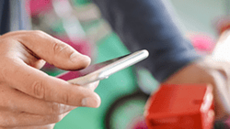 A person holds a smartphone in one hand and grips the handlebar of a red bicycle with the other, possibly unlocking or renting the bike using a mobile app.