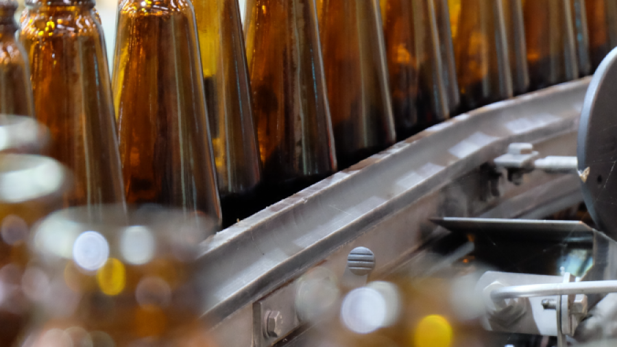 A row of empty brown glass bottles moves along a conveyor belt in a factory setting, ready for filling and packaging.