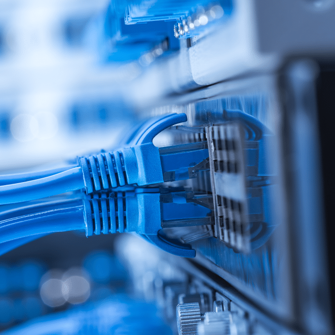Close-up of several blue Ethernet cables plugged into a network switch with blurred background components, depicting a data center or server room environment.