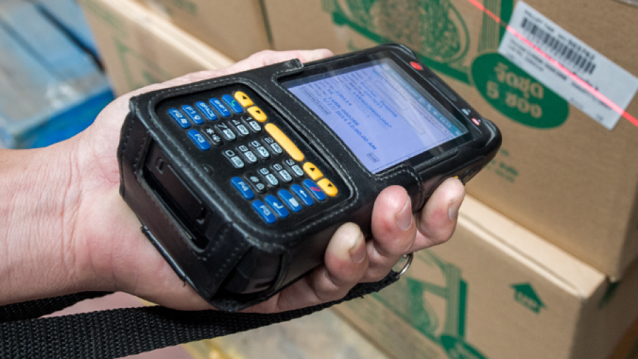A person uses a handheld barcode scanner to scan a barcode on a cardboard box in a warehouse setting.