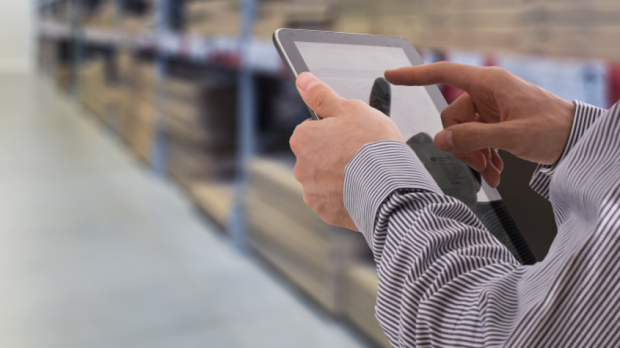 A person in business attire uses a tablet in a warehouse, showcasing distribution center automation, with shelves stocked with boxes in the background.