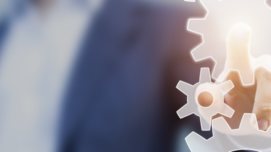 A person in a business suit is pressing a glowing gear icon on a transparent virtual touchscreen, symbolizing technology, Lean Process Improvements, or innovation. The blurred background emphasizes the focus on efficient process management.