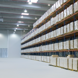 Large warehouse interior with tall racks filled with stacked pallets of goods. The space is brightly lit, featuring warehouse design consulting elements like high ceilings and spacious, clean floors for efficient storage and movement.