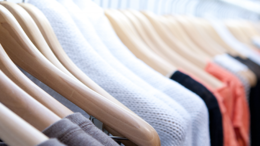 A row of assorted sweaters in neutral and muted colors hangs neatly on wooden hangers on a clothing rack.