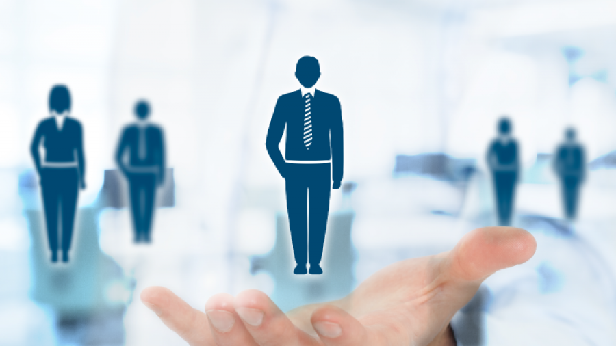 A person holds out their hand with digital icons of business professionals, representing recruitment or talent selection, overlaid on a blurred office background.