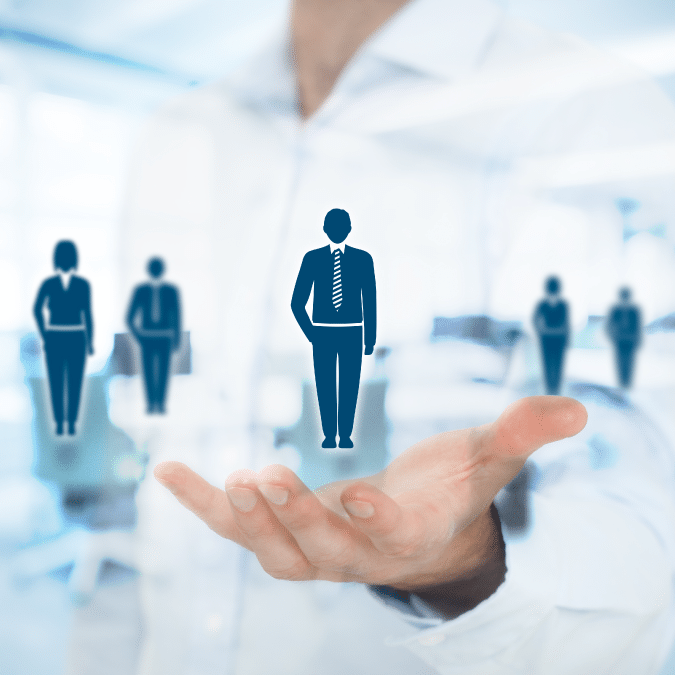 A person holds out their hand with digital icons of business professionals, representing recruitment or talent selection, overlaid on a blurred office background.