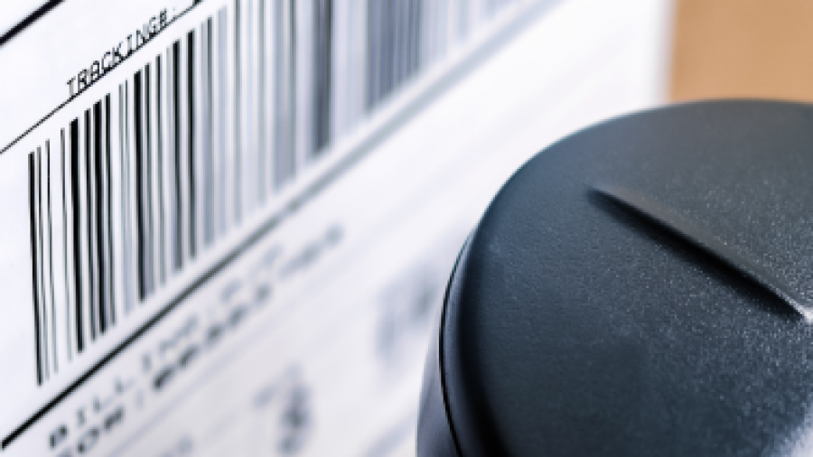 Close-up of a shipping label with a barcode on a cardboard box, next to a black scanner or device positioned for reading the barcode.