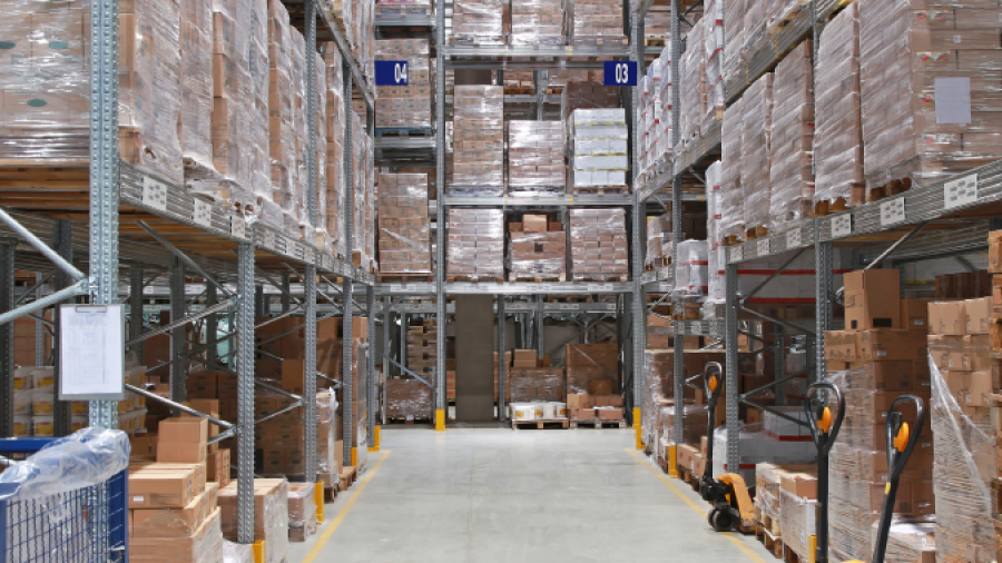 A warehouse aisle lined with tall shelves stacked with pallets of boxes and goods showcases efficient warehouse design consulting. Three pallet jacks are visible on the right, and the floor is clear for movement and storage operations.