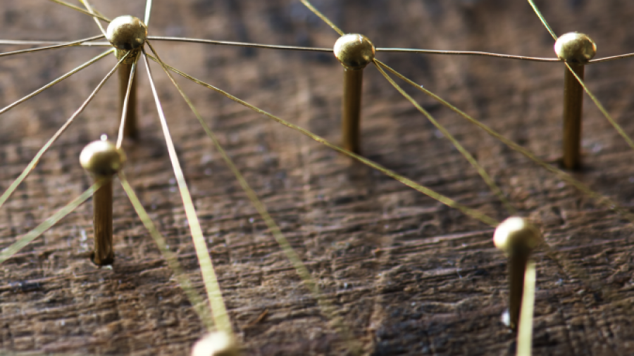 Close-up of brass pins connected by thin golden threads on a wooden surface, forming an abstract network or web pattern.