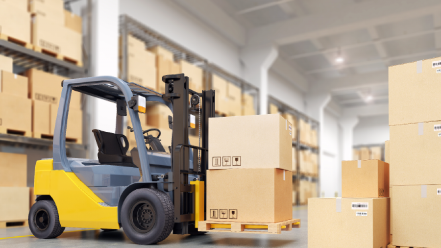A yellow and gray forklift moves a pallet of cardboard boxes inside a warehouse filled with shelves stacked with more boxes.