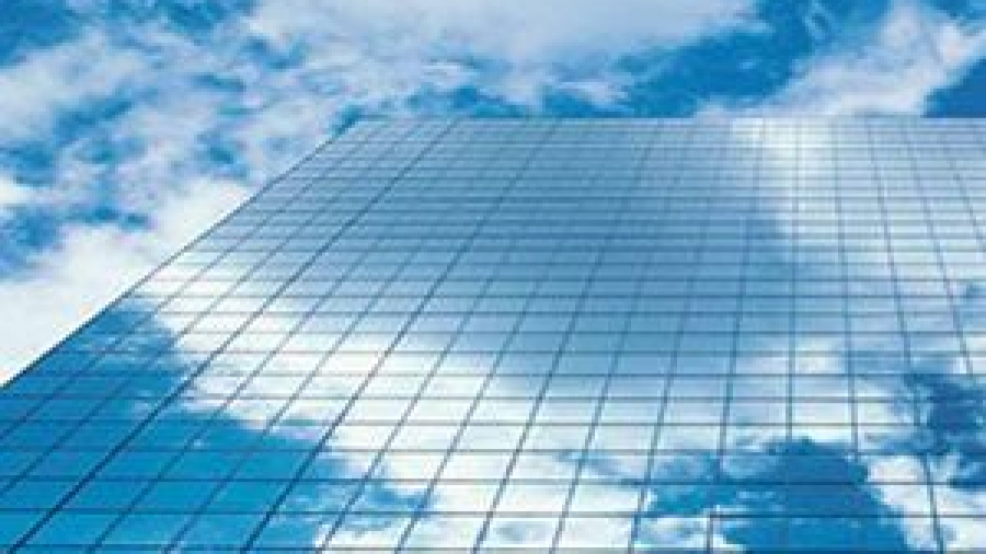 A tall glass building reflects a blue sky with white clouds, creating an almost seamless blend between the architecture and the sky above.