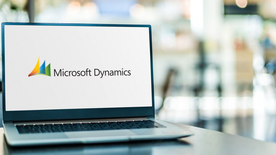 A laptop on a table displays the Microsoft Dynamics logo on its screen, with a blurred background of an office or cafe setting.