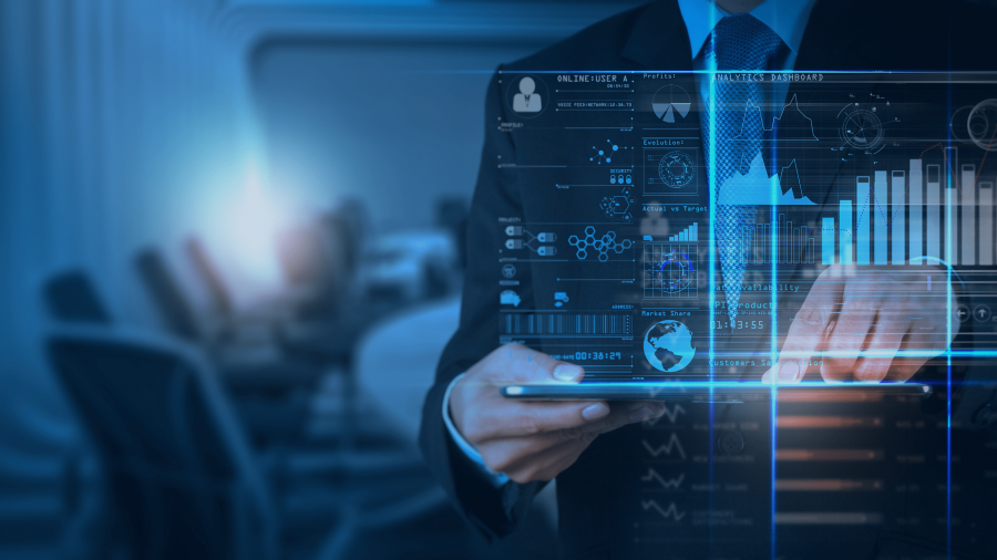 A person in a suit uses a tablet with virtual data graphics and charts overlaying the screen, representing modern business technology and data analysis in an office setting.