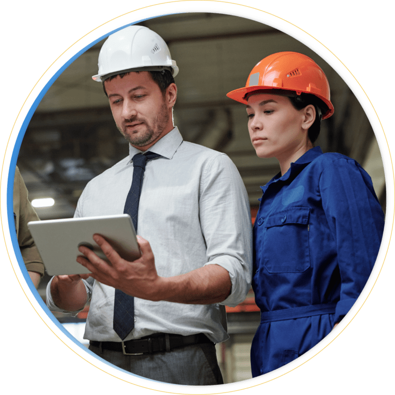 Two people wearing safety helmets and work clothes stand indoors. One holds a tablet, explaining Business Continuity Solutions to the other, who listens attentively in an industrial or construction setting.