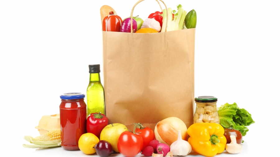 A paper grocery bag filled with fresh vegetables, surrounded by tomatoes, bell peppers, garlic, and more—perfectly arranged to highlight smart distribution consulting for quality produce on a white background.