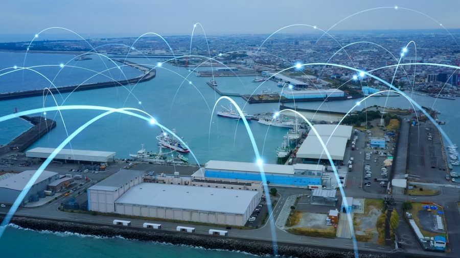 Aerial view of a port city with shipping docks and warehouses, overlaid with digital lines and points representing data communication or a responsive supply chain network.