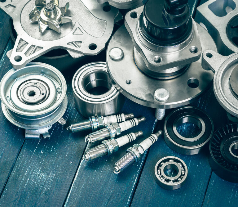 Assorted car engine parts, including spark plugs, bearings, pulleys, and metal components, arranged on a blue wooden surface.