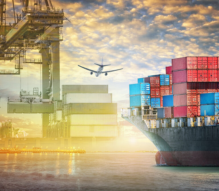 A cargo ship loaded with colorful shipping containers is docked at a port. Overhead cranes move containers, and an airplane flies above, illustrating global trade, logistics, and the efficiency of an agile supply chain.