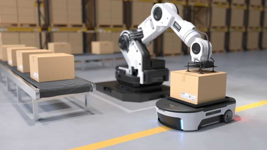 A robotic arm places a cardboard box onto an autonomous mobile robot in a warehouse, showcasing the future of supply chain; more boxes are lined up on a conveyor belt and shelves filled with boxes are in the background.