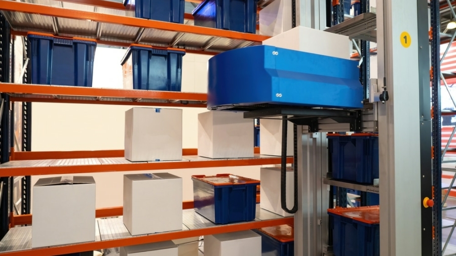 Automated warehouse system with a robotic arm handling white boxes on metal shelves, surrounded by blue storage bins in an organized industrial storage area.