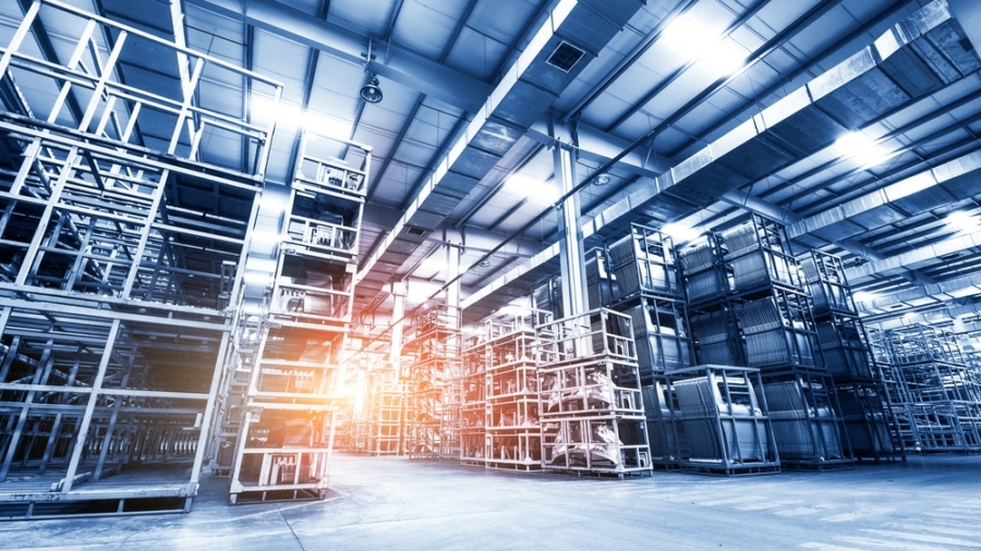 Large, modern warehouse interior with tall metal storage racks and wide aisles, optimized for slam line automation. Bright lighting and a warm sun flare fill the facility, creating a clean, organized atmosphere.