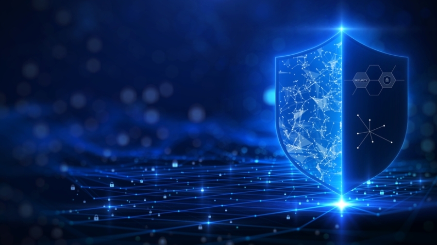A glowing blue shield with digital network patterns stands on a grid-like surface, symbolizing cybersecurity, Microsoft application management, and data protection, with abstract hexagons and connections in the background.