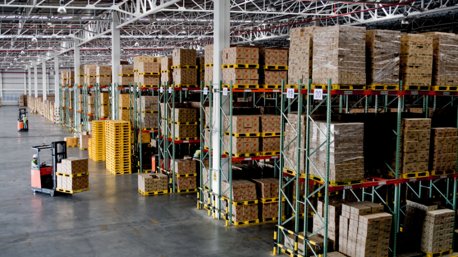 Large warehouse with high shelves stocked with boxes. Two forklifts move through the spacious, well-lit area, transporting goods. Efficient slotting ensures rows of pallets and organized inventory fill the industrial space.