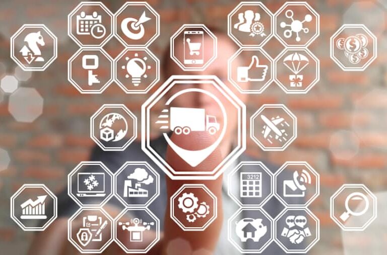 A person touches a transparent screen displaying interconnected hexagonal icons related to supply chain and logistics, including a truck, charts, gears, and delivery symbols, with a blurred brick wall in the background.