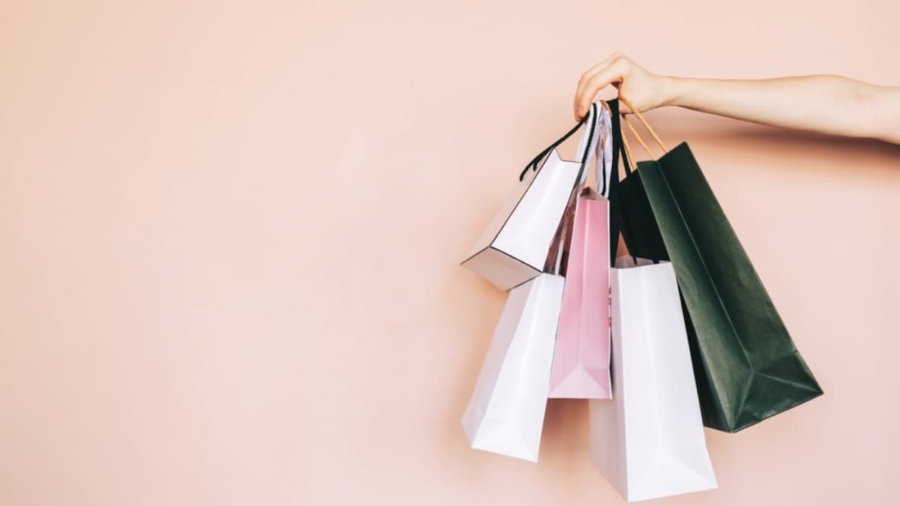 A hand holding several colorful shopping bags—perfect for showcasing WMS solutions—stands out against a light peach background. The bags, in white, pink, and green, vary in size and create a vibrant display.