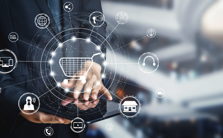 A person in a suit uses a tablet, with a digital overlay of a shopping cart icon surrounded by various e-commerce and technology icons, representing online shopping and digital business concepts.