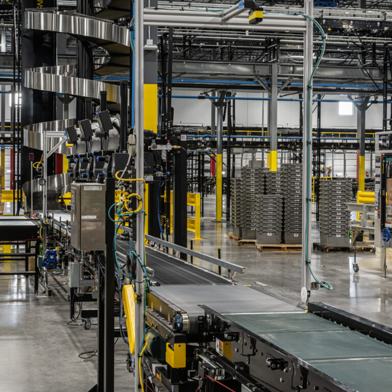 A modern warehouse interior featuring slam solutions, with conveyor belts, stacked cardboard boxes, metal shelves, and various machinery, all under bright industrial lighting.