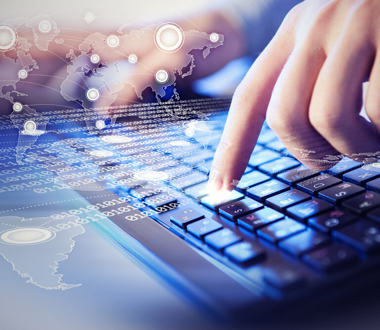 A person’s fingers typing on a computer keyboard with a digital overlay of a world map, binary code, and network connections, symbolizing global technology and data communication.