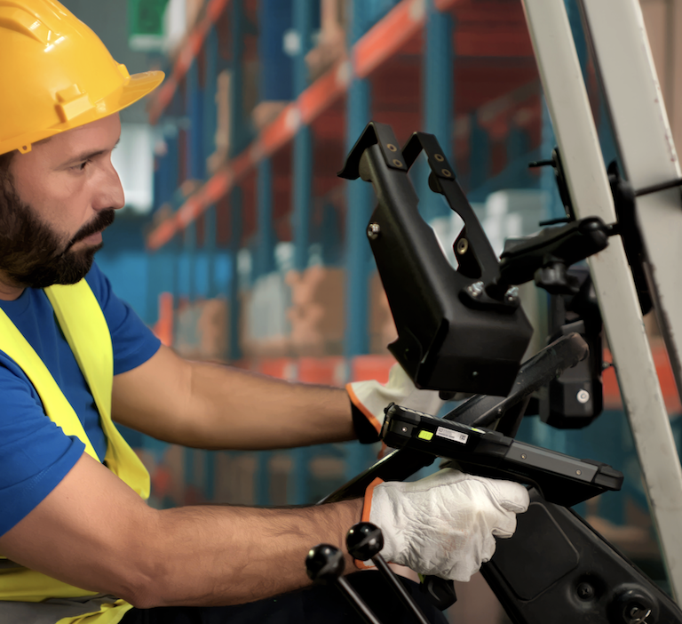A warehouse worker wearing a yellow hard hat, reflective vest, and gloves operates a forklift inside an ERP-managed storage facility with shelves of boxes in the background.