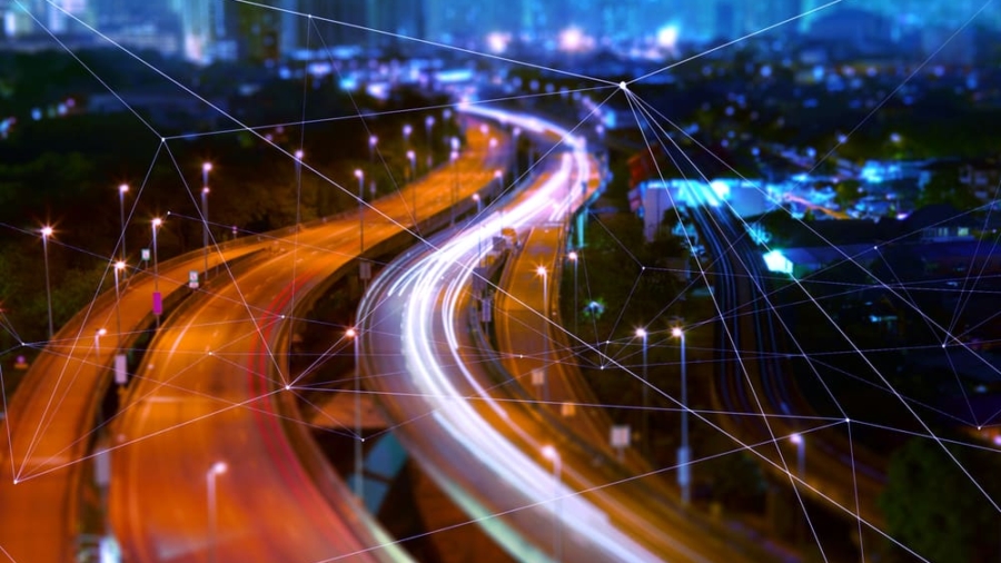 A blurred, colorful night view of a city highway with vehicle light trails. Overlaying digital network lines evoke connectivity, technology, and the flow of an OMS—all central to understanding what is supply chain strategy in urban environments.
